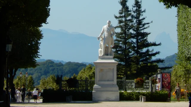 Statue of a person on a pedestal in a park with trees and mountains in the background