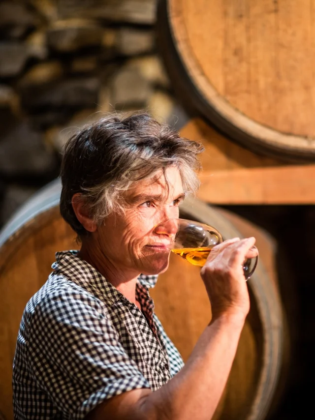 A woman tasting wine in front of wooden barrels